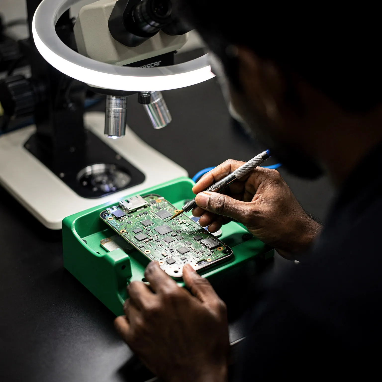 Illustration: technician working on a phone logic board under a stereo microscope